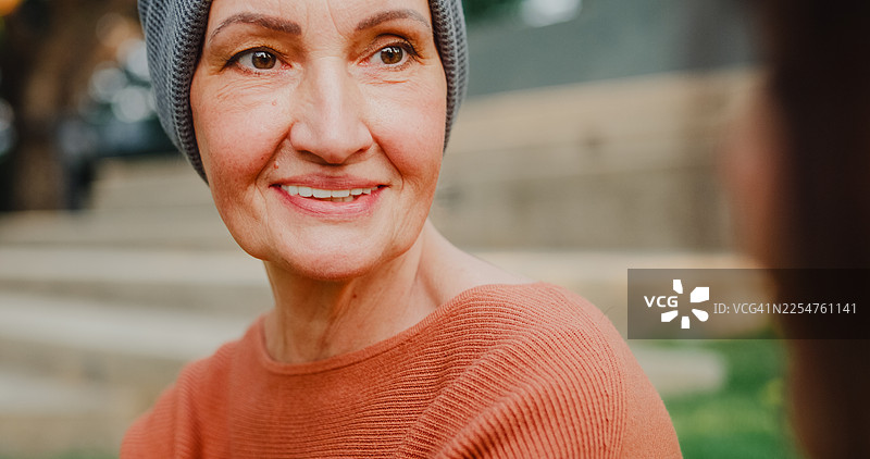 老年女性癌症患者戴着头巾，与看护者在公园户外进行情感支持、治疗和康复。癌症生存概念。图片素材