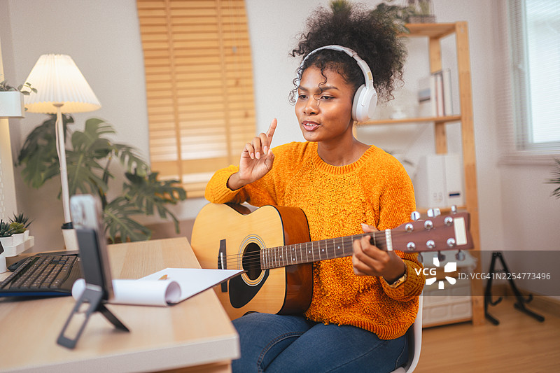 年轻女子戴着耳机在线教授吉他课程，通过引人入胜的虚拟课程促进远程音乐教育和互动。图片素材