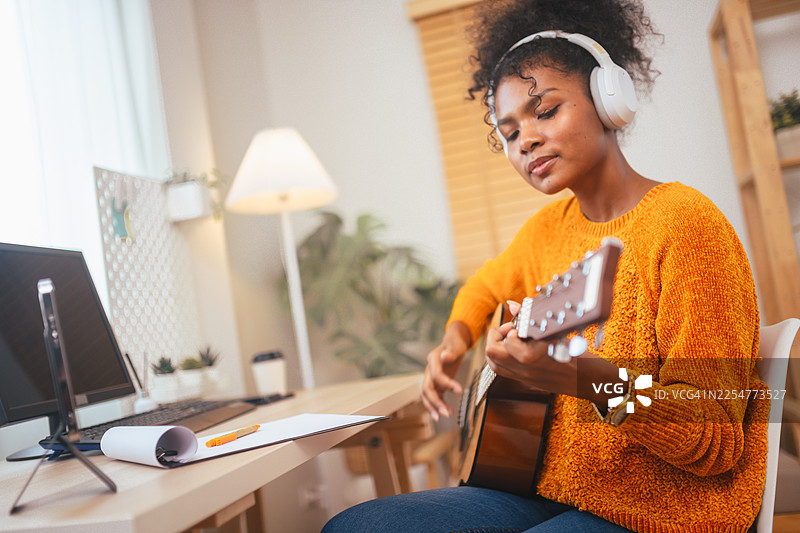 一位女性在家里的办公室里戴着耳机弹奏原声吉他，磨练音乐技巧。这是理想生活方式和创造力的概念。图片素材