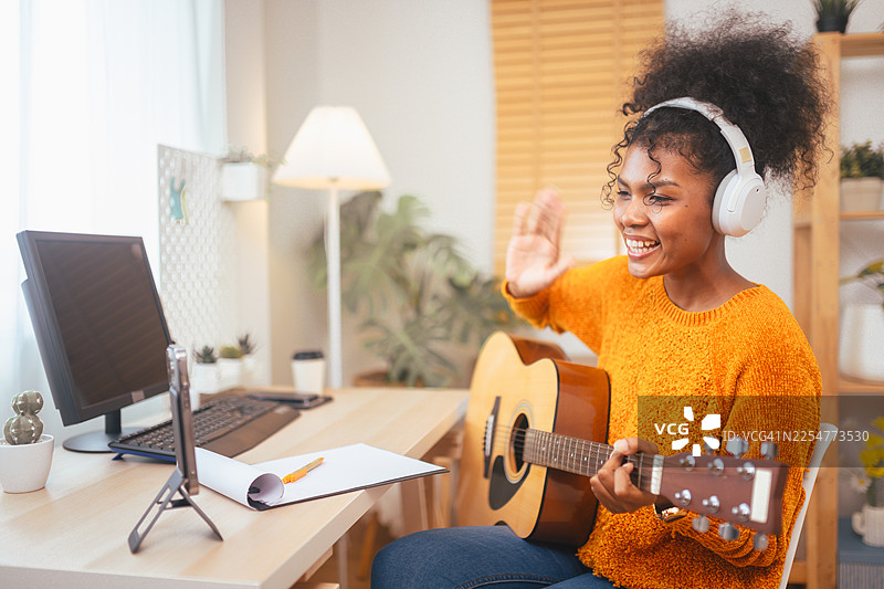 年轻女子在舒适的房间里，戴着耳机弹吉他，通过电脑学习在线音乐课程，提升技能。图片素材