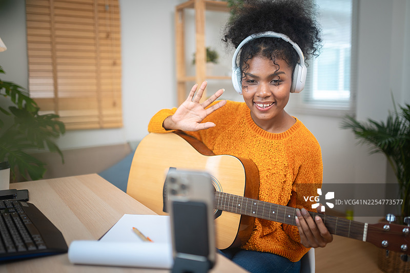 年轻女子戴着耳机，在线上课程中弹奏吉他，体现了虚拟音乐学习和创意技能的发展。图片素材
