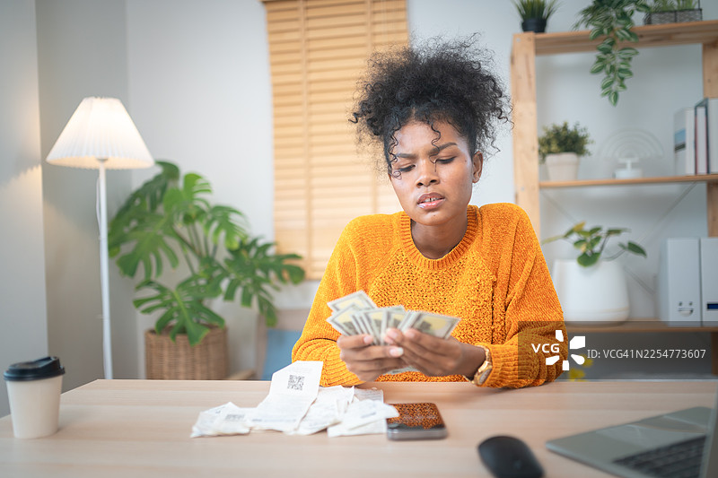 年轻女子在家中的办公桌前数着现金，在舒适现代的环境中有效管理个人财务。图片素材