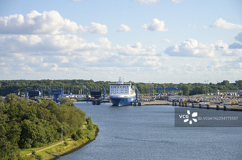 德国石勒苏益格-荷尔斯泰因州吕贝克特拉弗明德斯堪的纳维亚港,停泊着芬兰航运公司的巨型渡轮,周围是水和蓬松的云朵图片素材
