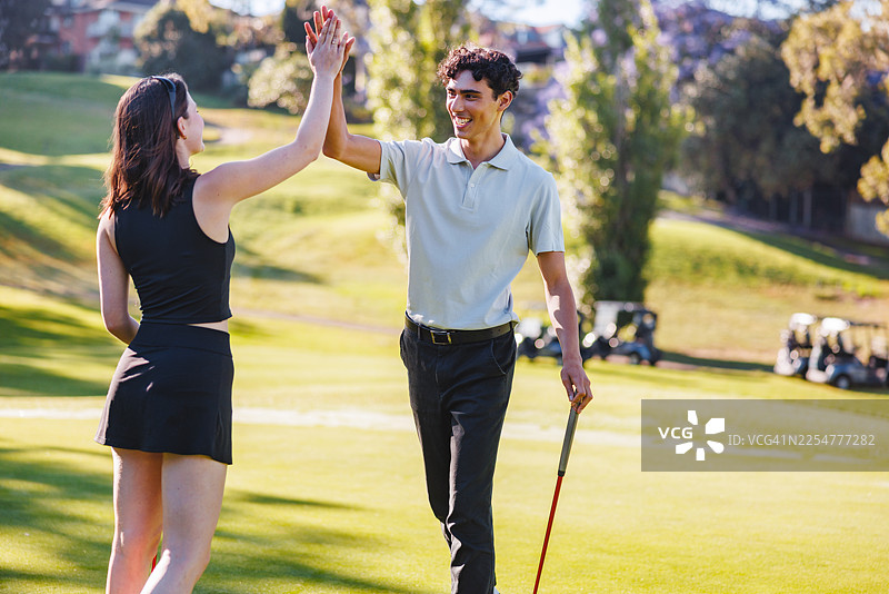 欣喜的年轻白人情侣在高尔夫果岭上击掌图片素材