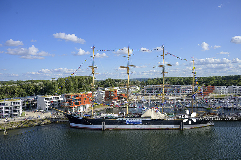 在蓝天下,特拉弗明德、吕贝克、石勒苏益格-荷尔斯泰因州,现代建筑前,停泊着传奇四桅帆船“帕萨特”号以及众多船只,构成一幅港口美景。图片素材