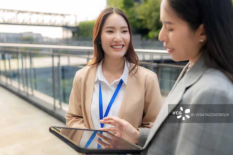 微笑的同事们在现代办公室里通过平板电脑讨论商业策略。专业的团队自信高效地协作，以实现企业成功和新业务增长。图片素材