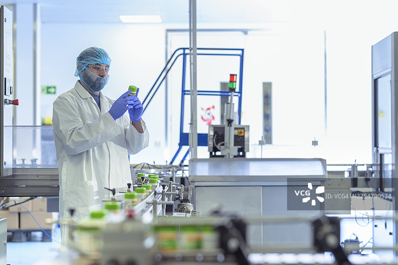 制药厂的包装线上，一名工人正在检查药瓶图片素材
