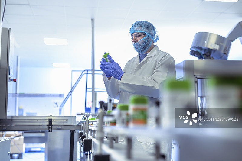 制药厂的包装线上，一名工人正在检查药瓶图片素材