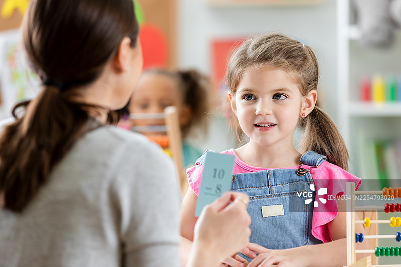 年轻女孩在教室里与老师一起积极学习数学，旁边有一个算盘。图片素材