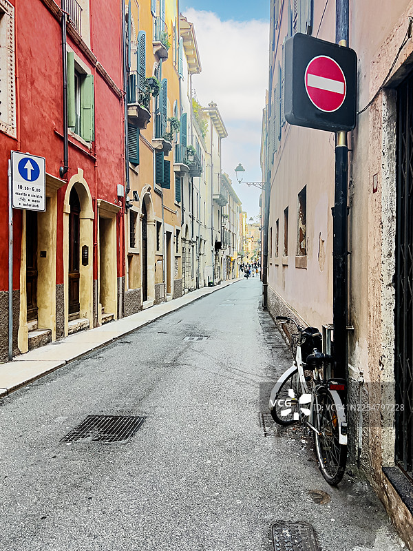 意大利维罗纳市中心一条安静空旷的街道，街道两旁是典型的色彩鲜艳的房屋，停放着一辆自行车，还有一个禁止停车标志以及一个仅限居民通行的车辆限行区标志。图片素材