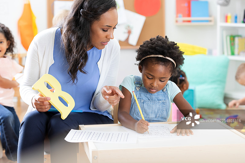 一位老师在明亮的教室里耐心指导一名年轻学生学习字母课。图片素材