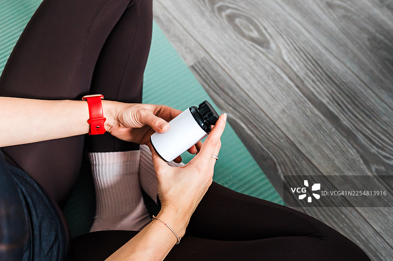 居家健身垫上运动后手持补充剂罐的女性图片素材