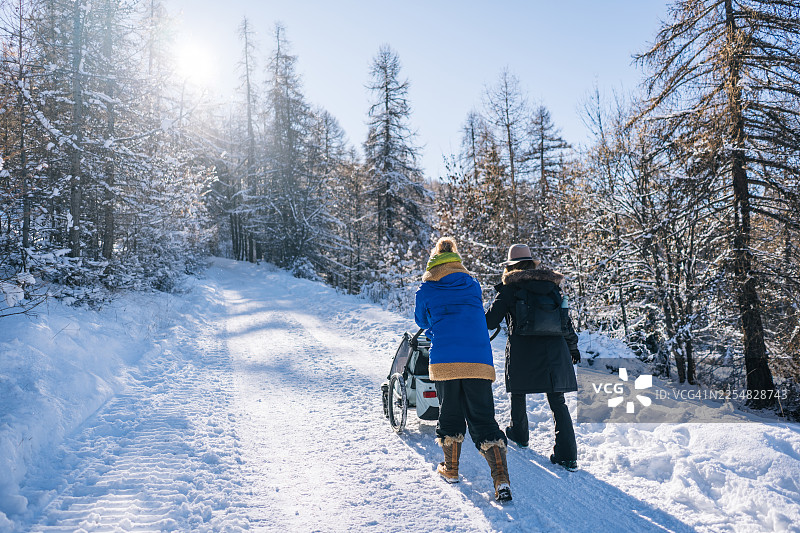 祖母和成年女儿在冬季的山路上推着婴儿车图片素材