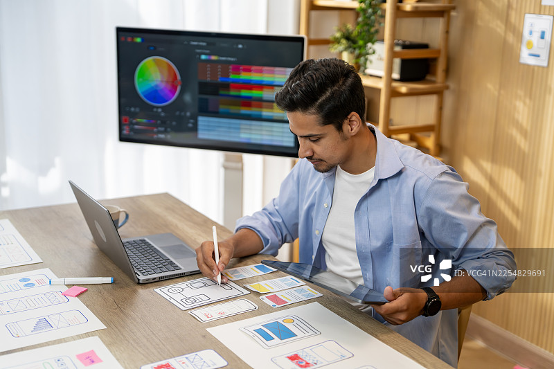 Young man creating mobile app wireframes at desk图片素材