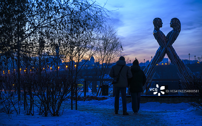 一对夫妇在基辅观看冬季日落，背景是“团结”雕像。图片素材