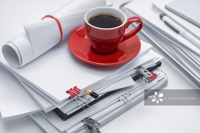 办公桌上放着红色的咖啡杯和白色的办公文具，充满许多纸张的办公室氛围，空白的笔记本。图片素材