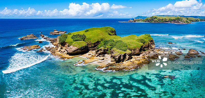 从空中俯瞰印度尼西亚龙目岛海岸，一处被绿意覆盖的岩石小岛被碧绿的海水和珊瑚礁环绕，呈现出宽广的全景。图片素材