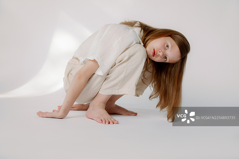身穿米色服装的年轻女孩摆出蹲姿，在白色影楼背景前，用于时尚和创意图片素材图片素材