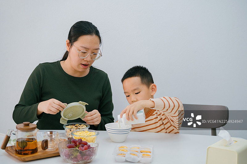 一位亚洲母亲在家中与她的两个孩子一起准备下午茶；亚洲家庭生活方式图片素材