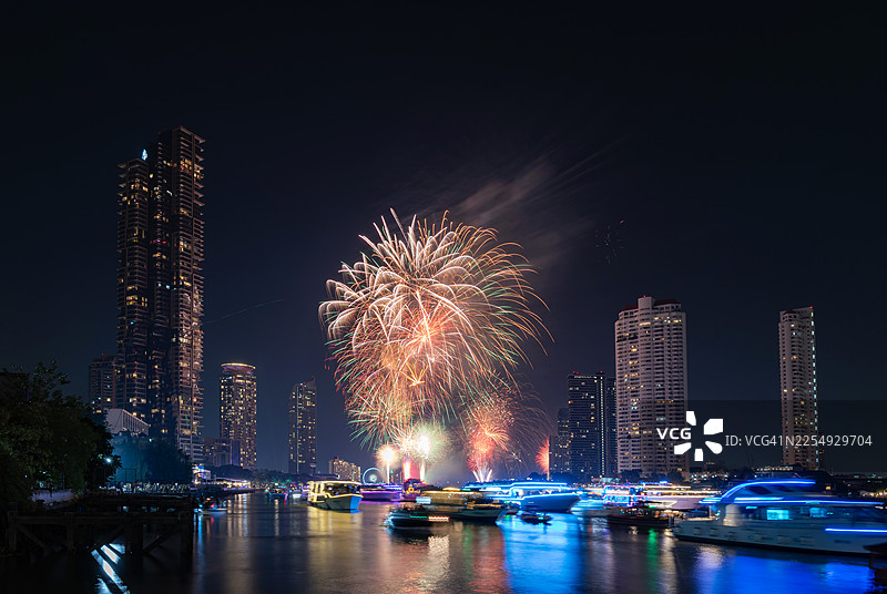 节日倒计时和新年庆典期间，河畔城市上空燃放的绚烂烟花。游客们在河上游船，观赏夜空中壮观的烟火表演。图片素材