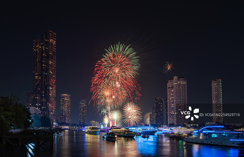 节日天际线 现代河流天际线上方的节日烟花表演，适用于圣诞节和新年活动。水面上闪耀的城市灯光、游船和烟火组成的唯美夜景。图片素材