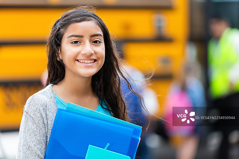 微笑着的年轻学生，手里拿着文件夹，站在校车前图片素材