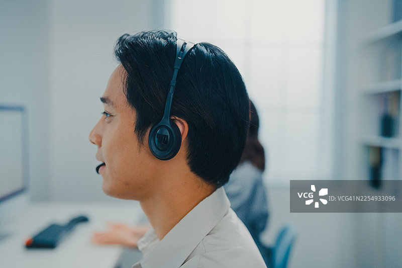 近距离拍摄的年轻亚洲客服代表佩戴耳机，正在帮助客户专员解决呼叫中心办公室的请求。专业数据中心工作。服务台操作员。图片素材