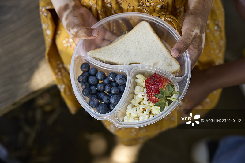 女孩拿着装有新鲜水果和零食的午餐盒图片素材