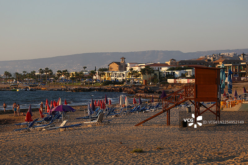 塞浦路斯海滩度假。帕福斯海岸线，木制救生员小屋，背景是模糊的山脉，金色时光。图片素材