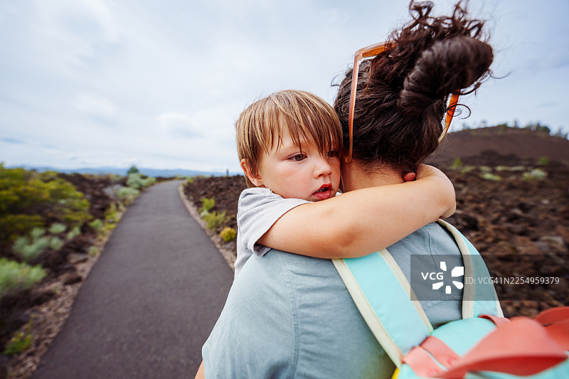 小男孩在家庭徒步时，靠在妈妈的肩膀上休息图片素材