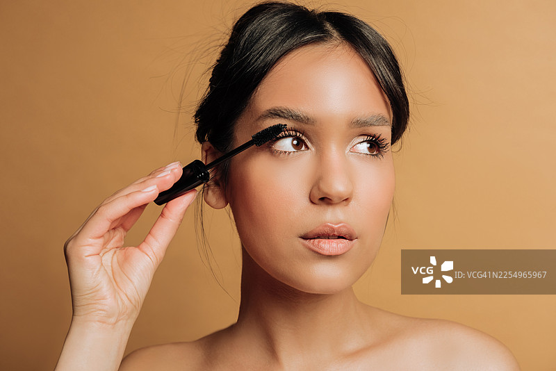 棕色背景下，一位美丽的女士正在使用睫毛膏拍摄的美容肖像。工作室拍摄。图片素材