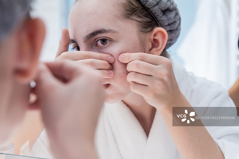 问题皮肤的真实写照：少女在浴室镜子前处理痘痘图片素材