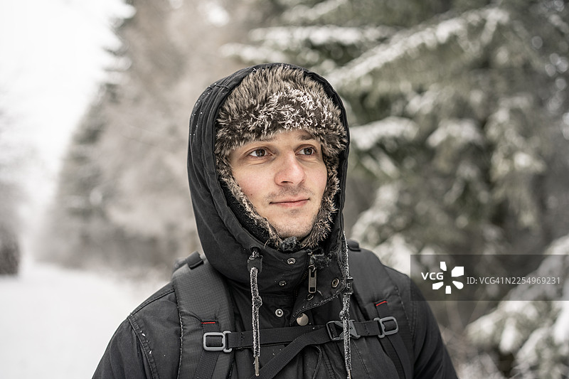 冬季冒险：身穿黑色派克大衣的男子在雪林中户外行走图片素材