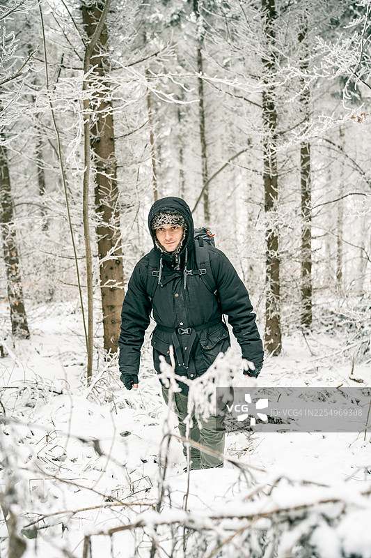 背着背包、穿着带帽夹克的男子在冬季雪林中徒步图片素材