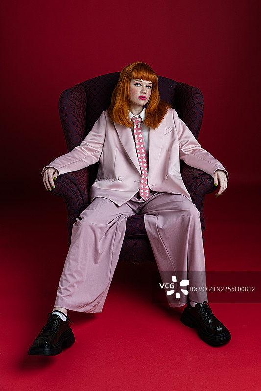 身穿粉色套装的女性，在单色背景的扶手椅上摆姿势图片素材