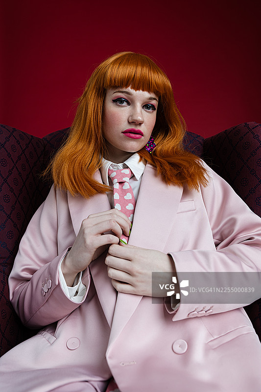 身穿粉色套装的女性在单色背景下的扶手椅上摆姿势图片素材