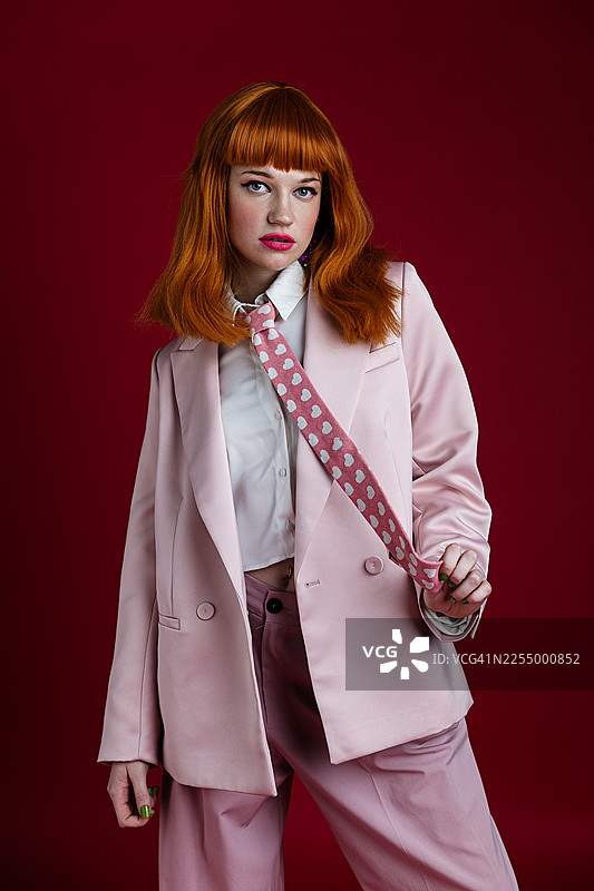 身穿粉色套装的时尚女子在纯色背景前摆姿势图片素材