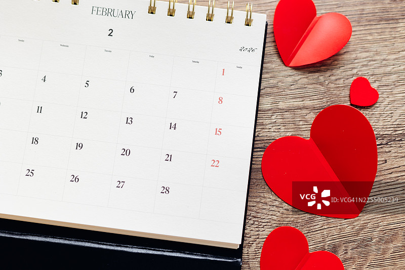 2026年2月的桌历，木质背景上装饰着红色的纸心。情人节概念。图片素材