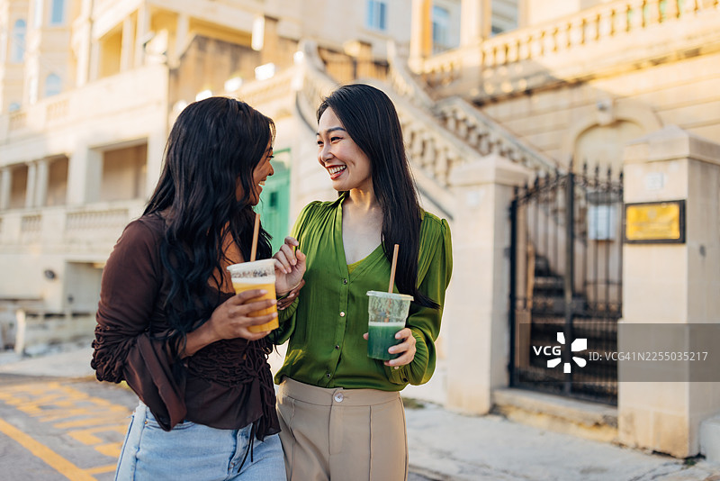 两位不同种族的朋友在历史悠久的城市街道上探索，手中拿着新鲜的冰沙图片素材