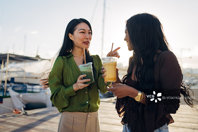 两位不同种族的朋友在水边喝健康的冰沙图片素材
