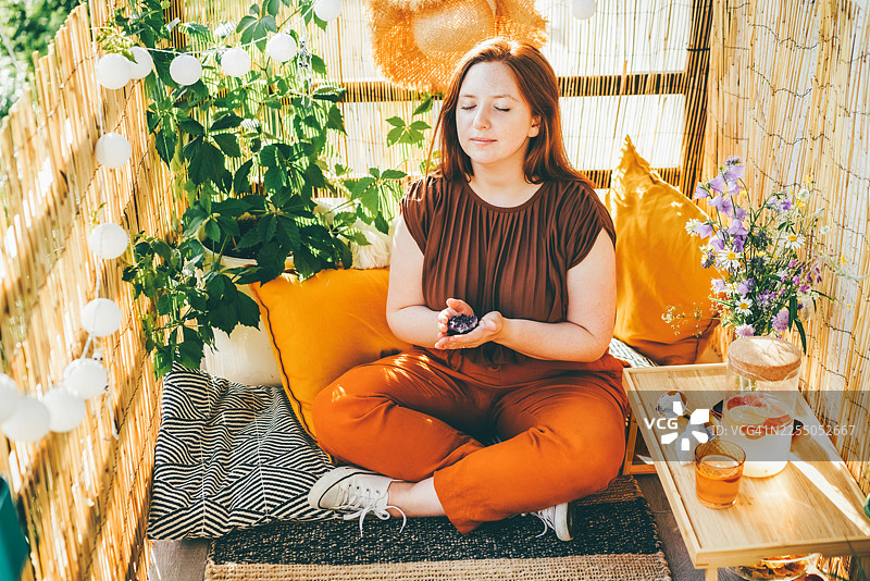 年轻女子在装饰阳光露台上，以莲花坐姿冥想，身旁摆放着闪亮的晶石。图片素材