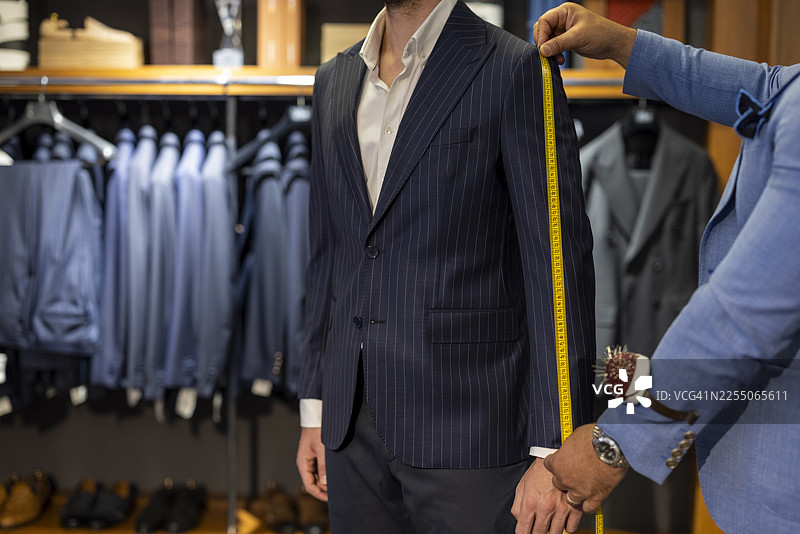 男装精品店里，裁缝正在为顾客量体定制西装图片素材