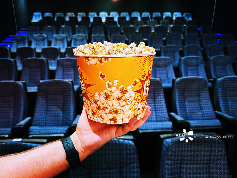 一个人在空荡荡的电影院里拿着一桶爆米花，个人视角图片素材