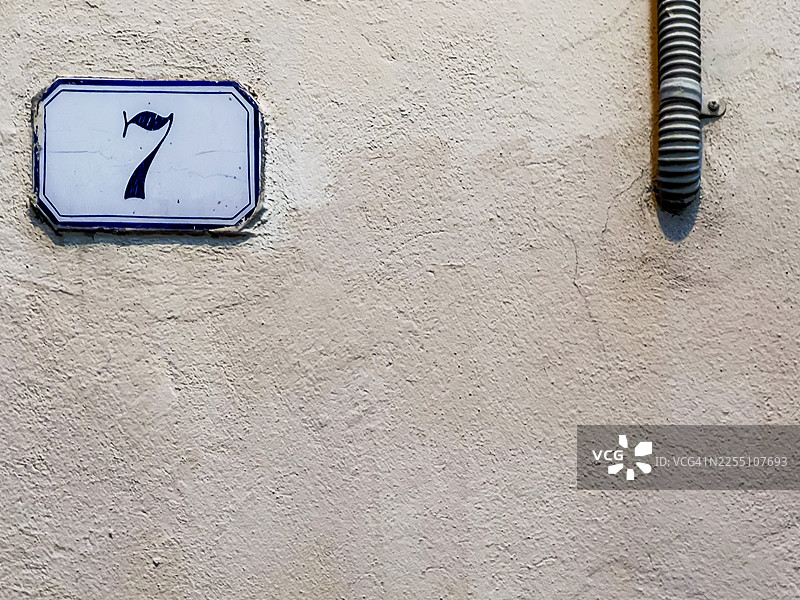 精致典雅的瓷质门牌号与粗糙的管道并列于同一面墙上，形成了鲜明的对比。图片素材