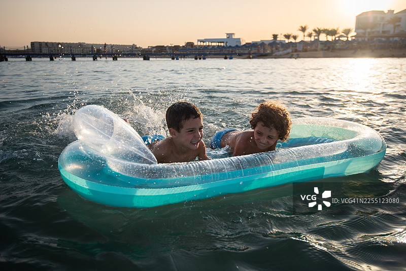 夏日度假日落时，两个年幼的兄弟在海上玩充气浮筏。图片素材