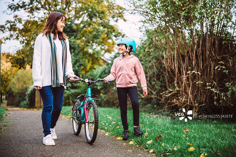 秋季公园里，母亲陪着女儿学习骑自行车图片素材