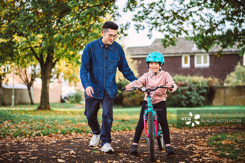 秋日公园里，父亲教女儿骑自行车图片素材