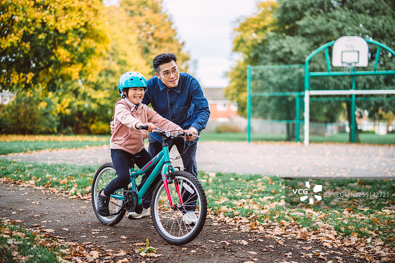 秋日公园里，父亲教女儿骑自行车图片素材