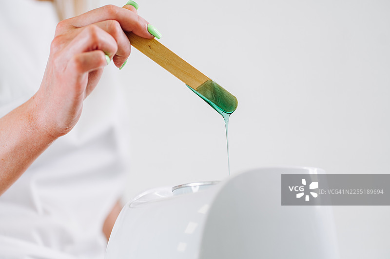 医务人员手持木制刮刀，绿色蜡油滴落图片素材