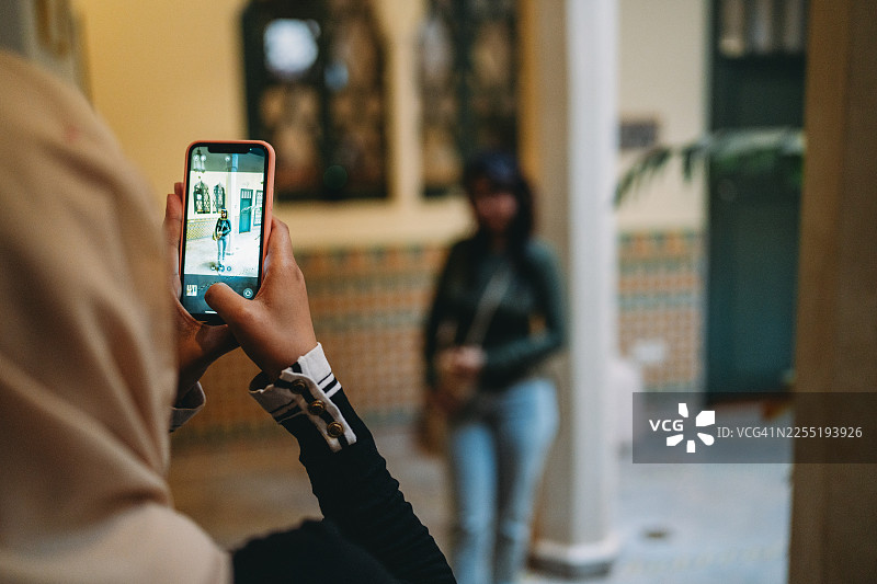 戴头巾的女士正在用智能手机给朋友拍照图片素材